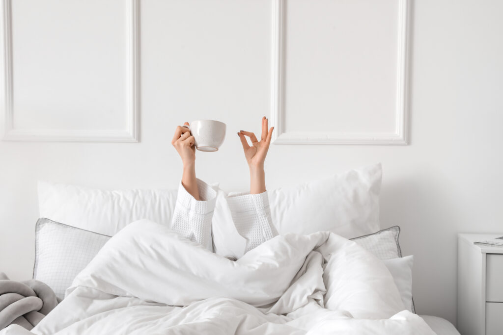 Person in bed holding a cup with one hand and showing 'OK' sign with the other