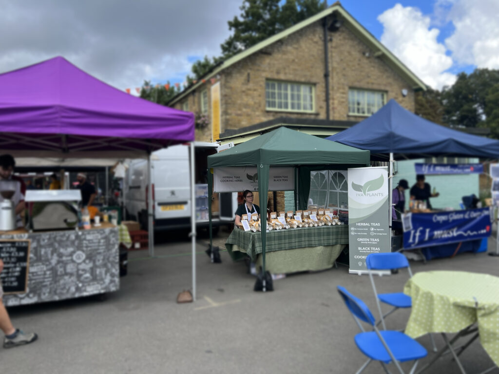 IVA Plants stall at Chiswick Food Market, surrounded by vibrant market atmosphere, offering herbal, Japanese green, and black Ceylon teas